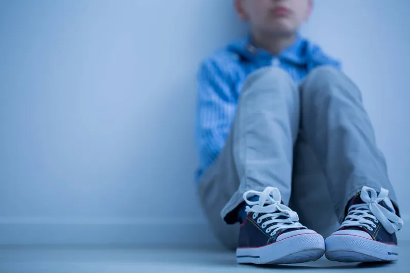 Jeune garçon assis par terre contre un mur, les genoux repliés