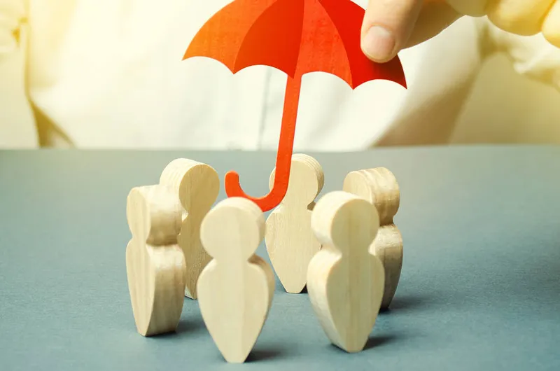Figurines en bois réunies sous un parapluie rouge, symbole de protection